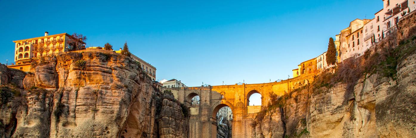 A city carved into the cliff with bright blue sky behind.