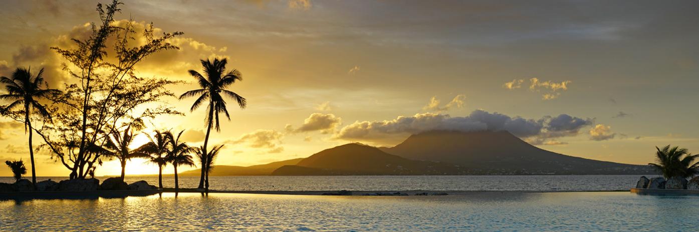 Sun setting over mountains through palms, reflecting off the ocean.