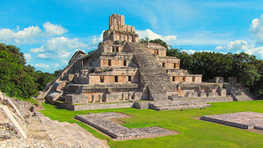 Ancient mayan ruins containing a large staircase surrounded by bright green grass.