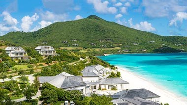 Lush greenery covers a large mountain leading into a white sand beach and bright turquoise water.