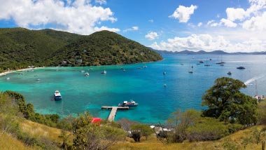 Bright shades of blue and turquoise water fill this white sand and mountain beach.