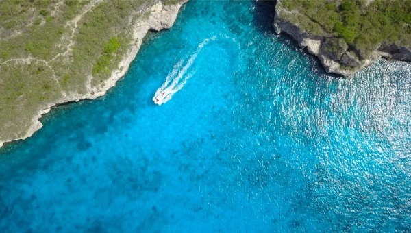 Bright blue water with a boat and wake, in front of green cliffs.