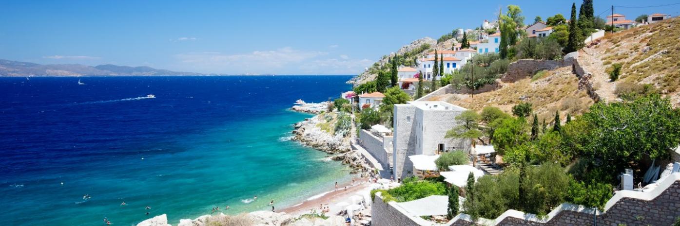 Blue green water before a sandy shore with old buildings.
