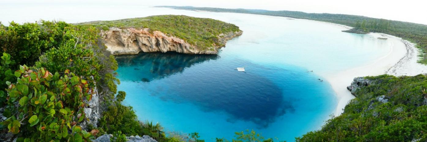 Dark blue hole in the midst of bright blue water surrounding by lush greenery.
