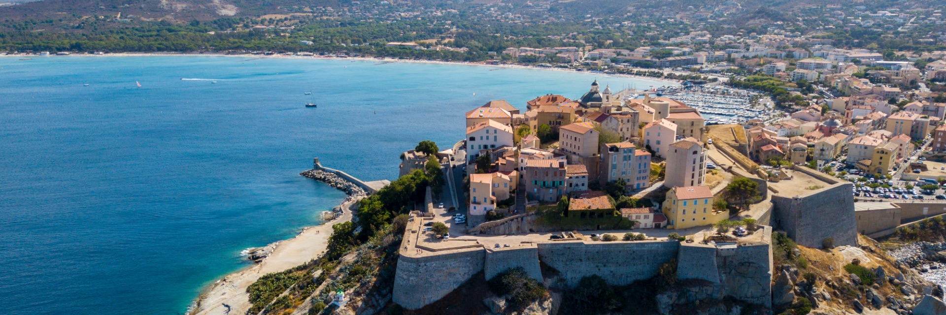 Old buildings surrounded by an old stone wall overlook the water.