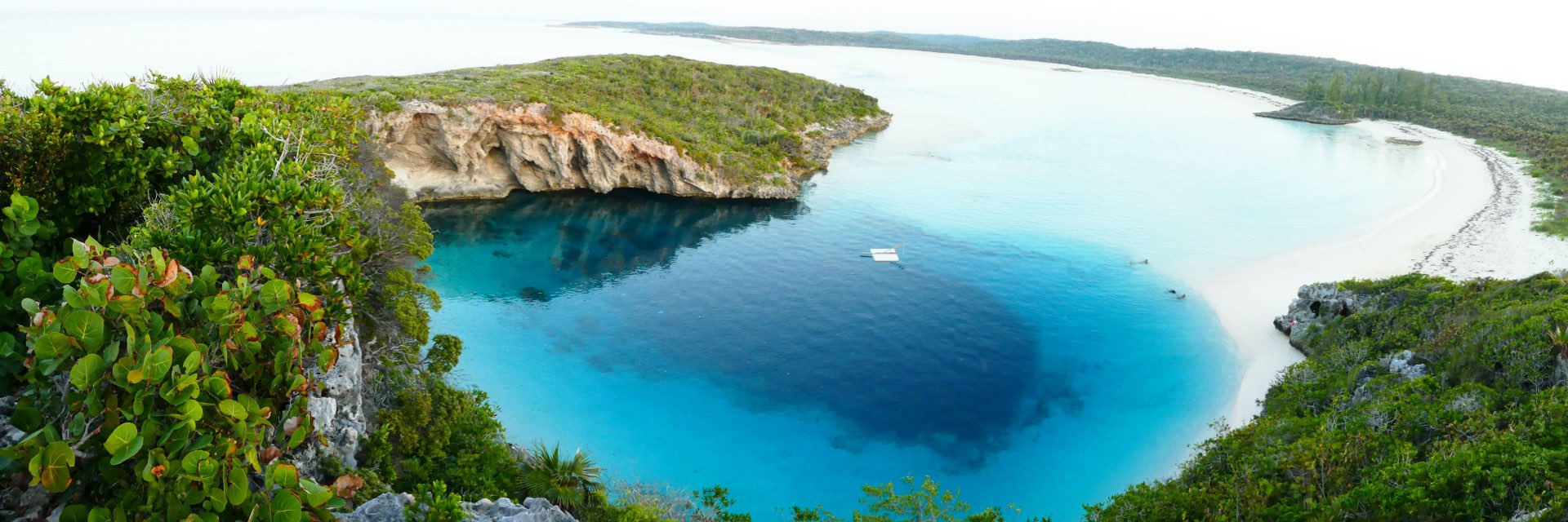 Dark blue hole in the midst of bright blue water surrounding by lush greenery.