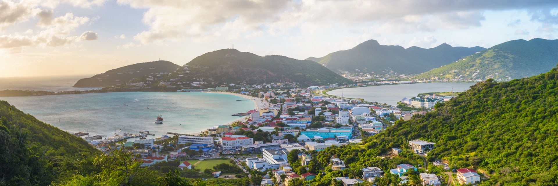 An aerial view of a colorful town surrounded by water and lush green mountains behind.