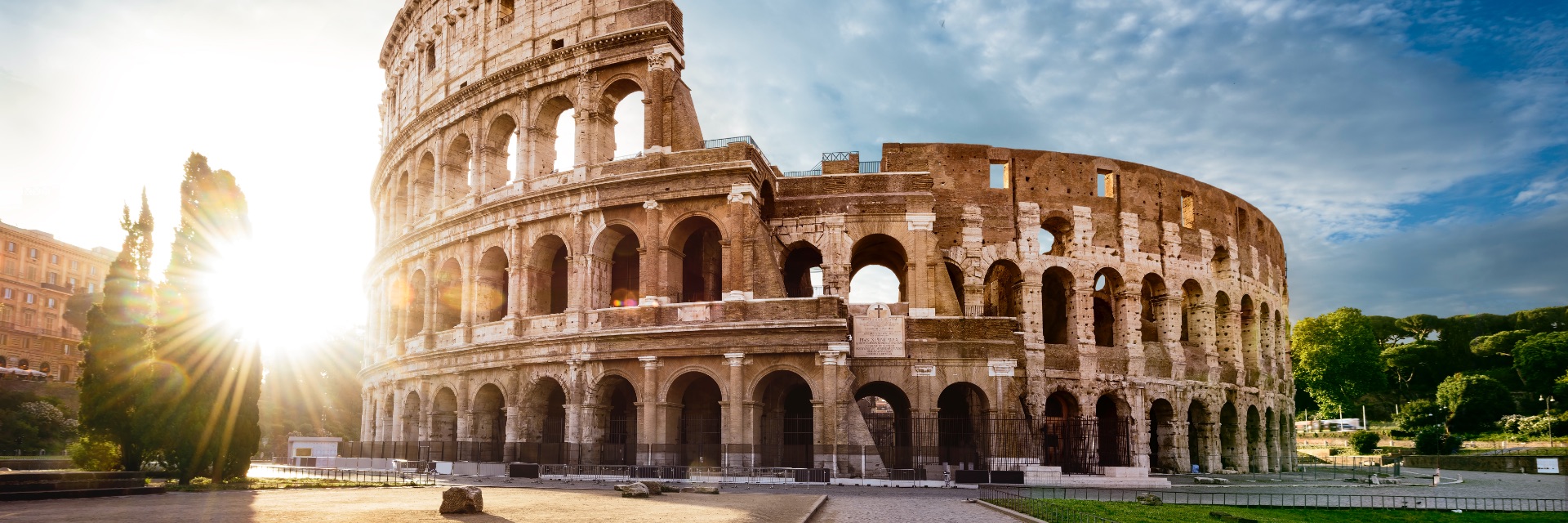A view of Rome's ancient Colosseum, with sun shining from behind.