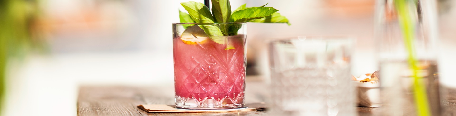 A pink cocktail in a rocks glass garnished with fruit and green herbs.