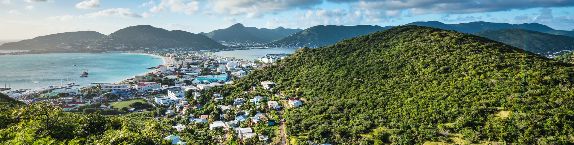 View from a lush mountain top looking over a small town surrounded by aquamarine waters.