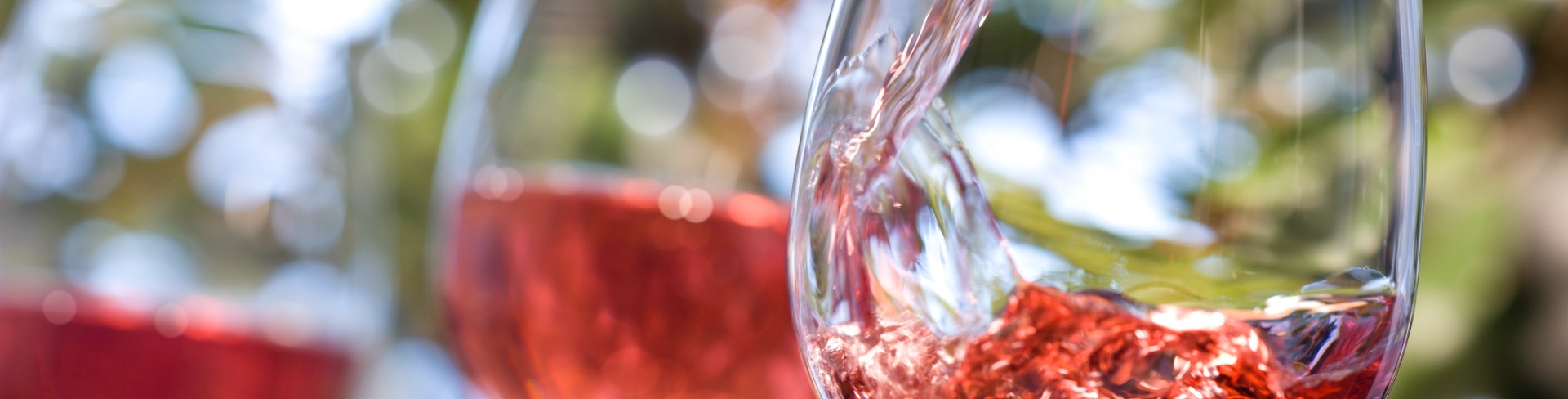 Wine glass in the foreground with pink wine being poured into the glass.
