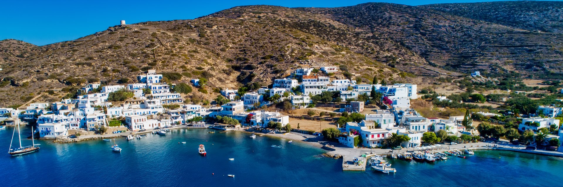 White stucco buildings with blue roofs on a hillside in front of the sea in Amorgos, Greece