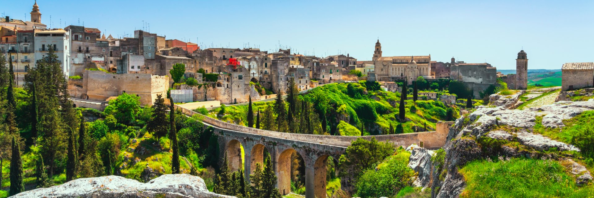 An aqueduct passes over a lush green valley, with the quaint city of Bari, Italy behind