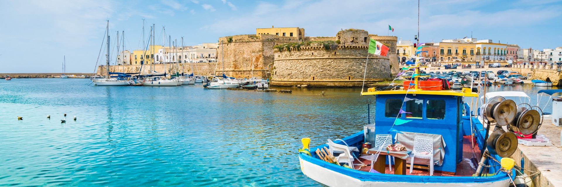 A white and blue boat floats in light blue water, with tall stone walls behind.