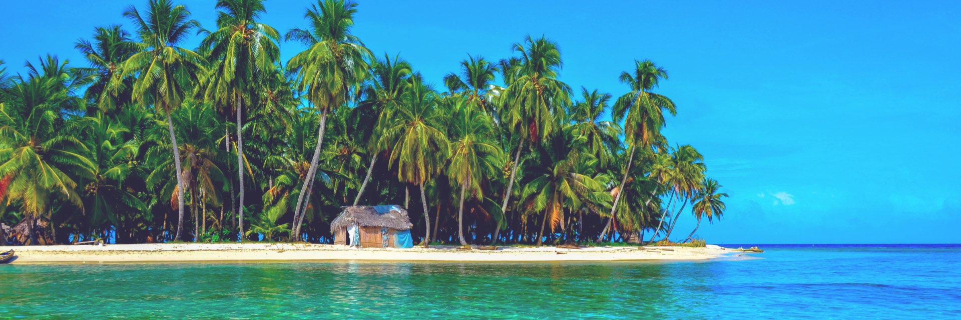 Small tropical island with thatched roof house, white sandy beach and blue waters.