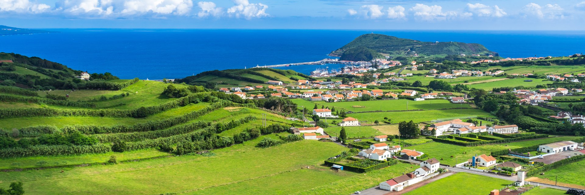 Aerial view of small village with white house and red roofs surrounded by beautiful rolling green hills with azure colored sea in bacakground.