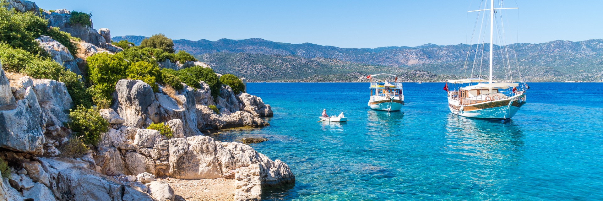 A boat sits in clear, bright blue water in front of a rocky shore.