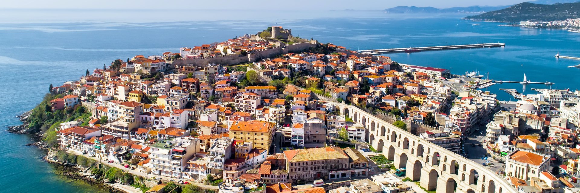 A bird soars over a town surrounded by water, with an ancient aqueduct winding through.