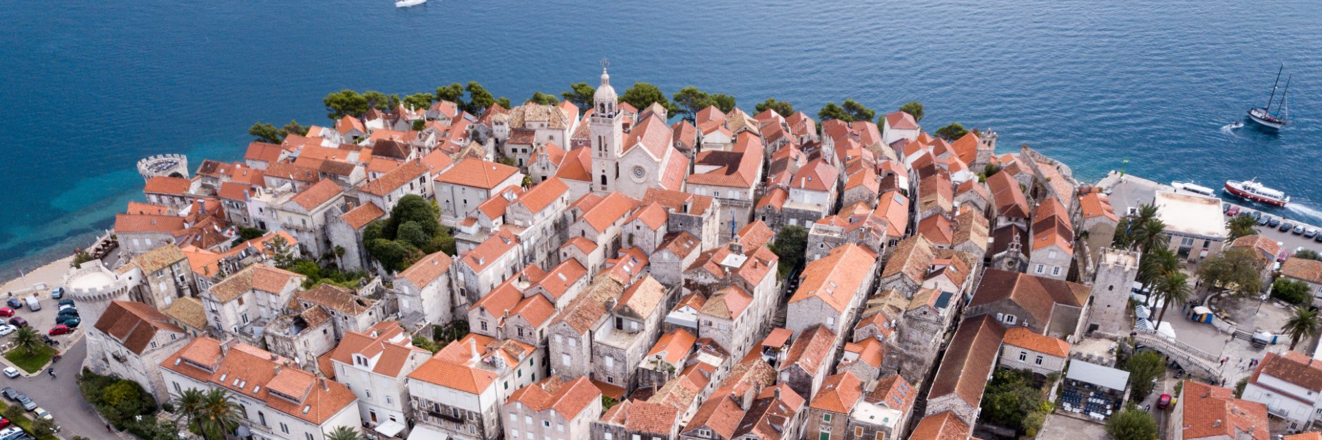 Aerial view of small seaside village with red roofs and blue sea in background.