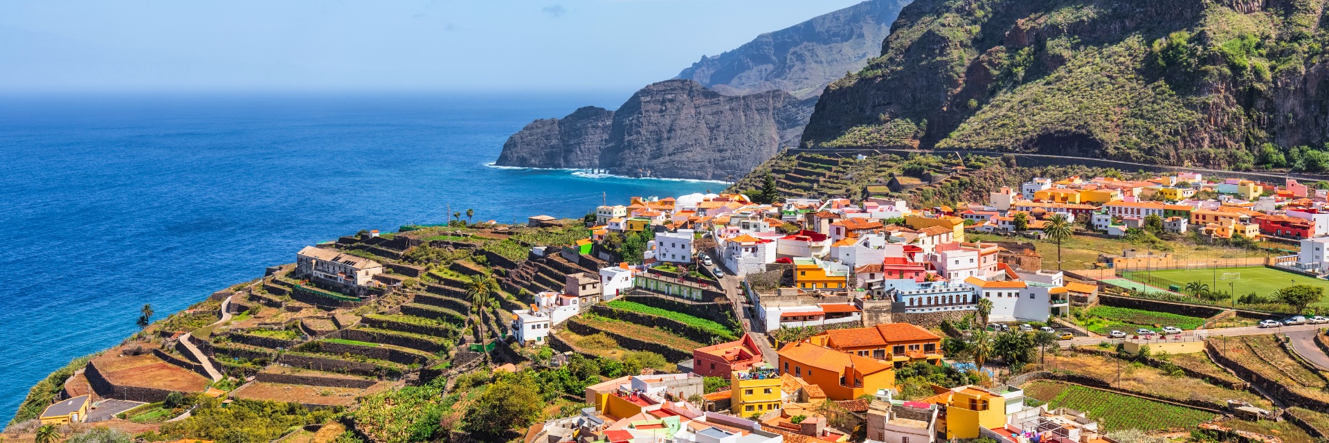 A cliffside town by the sea, filled with bright orange and white buildings and green landscape.