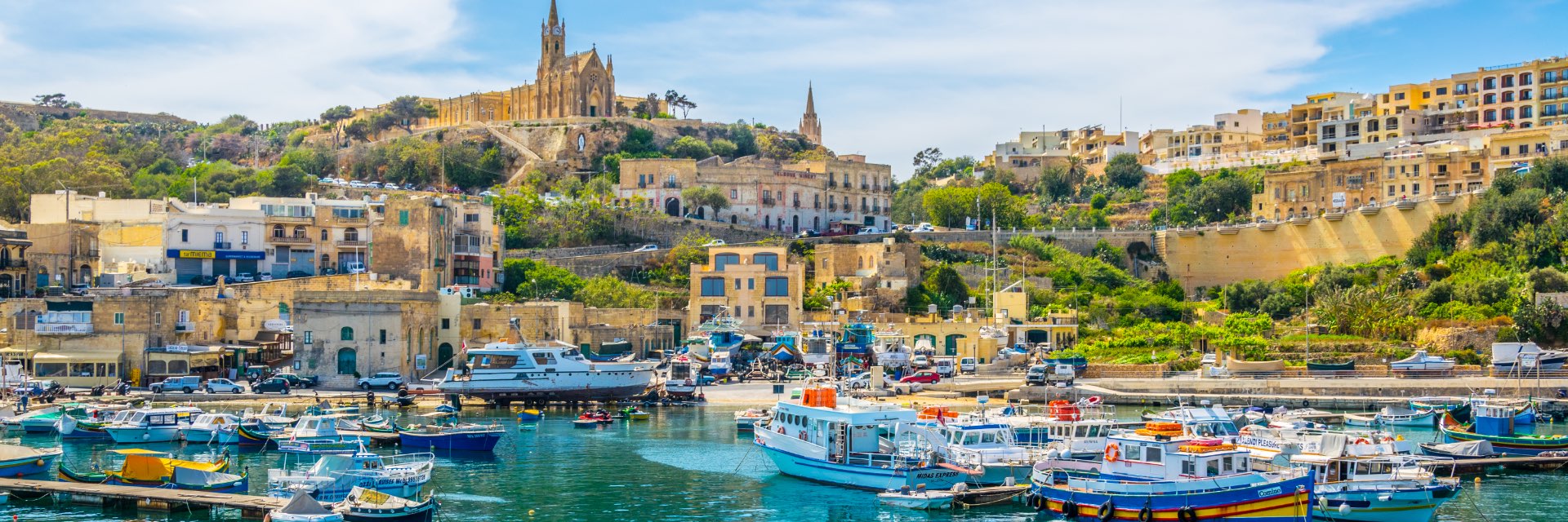 Marina with small boats and village and large cathedral in background.