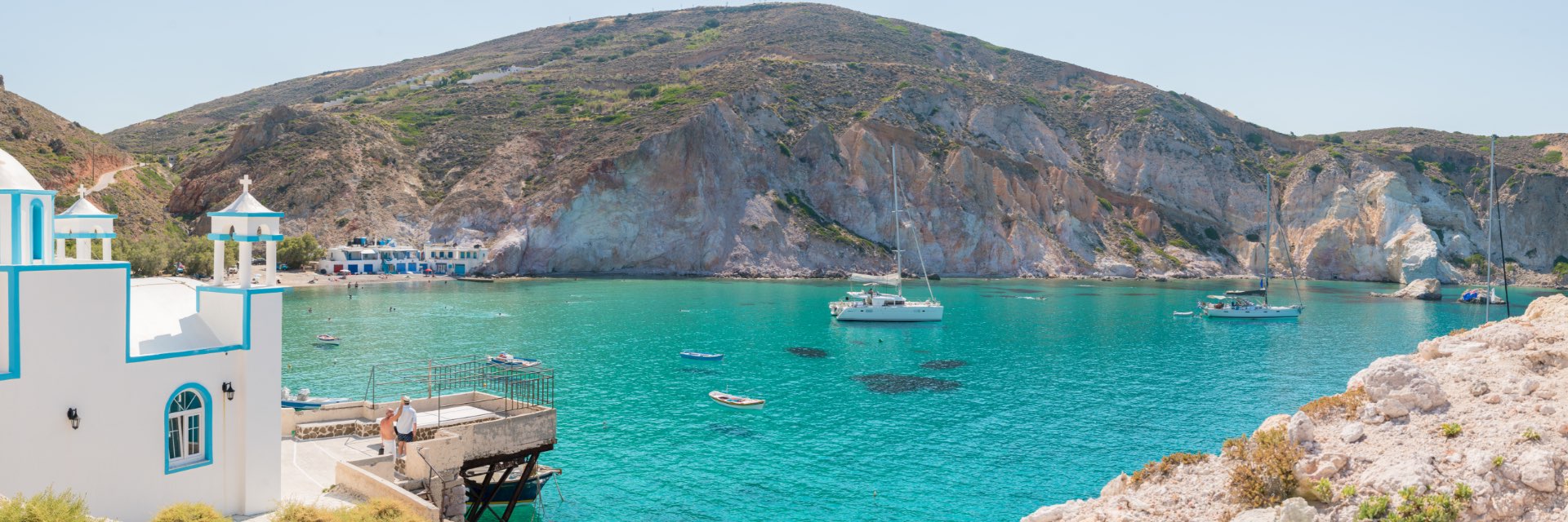 A boat sits in bright aqua water in front of a mountain.