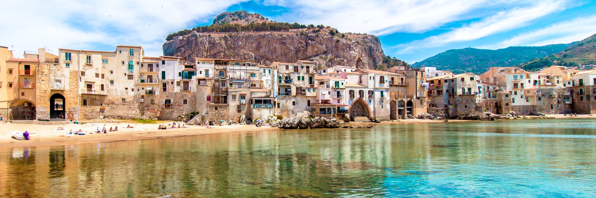 Blue green water before a sandy shore with old buildings.