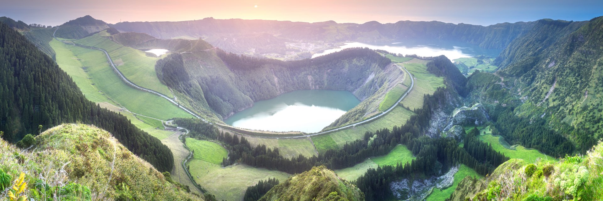 Birdseye view of multiple lakes surrounded by hills and greenery with sun setting in the background.