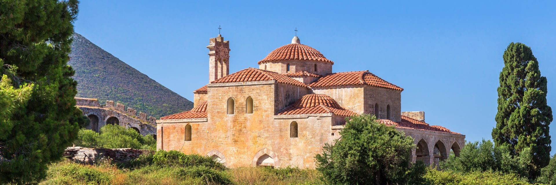 An orange house on a green hill surrounded by trees and blue sky.