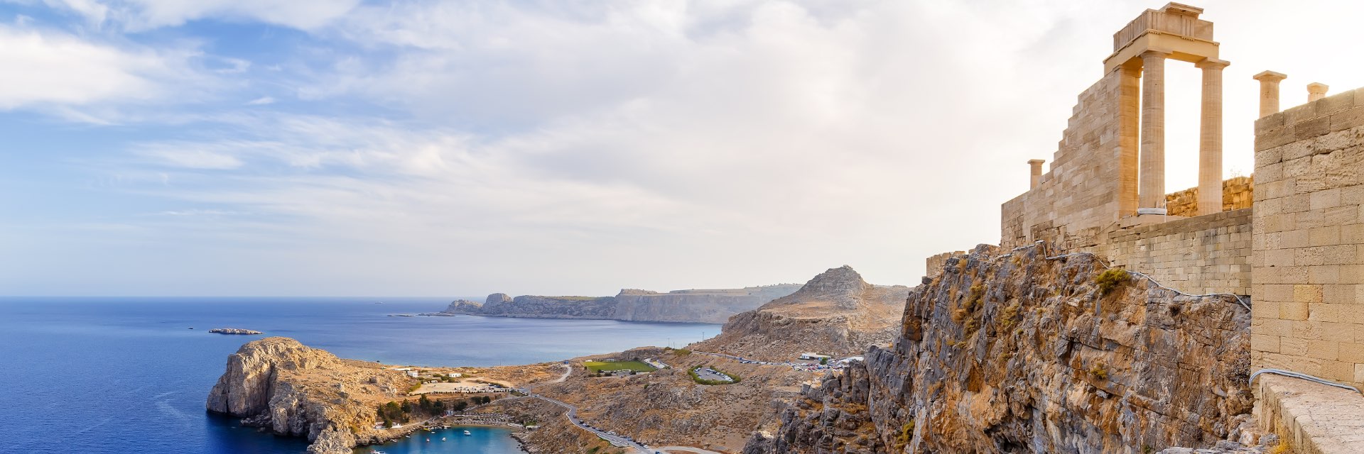 Deep blue water along the rocky coast, with a ruins on top of the cliff.