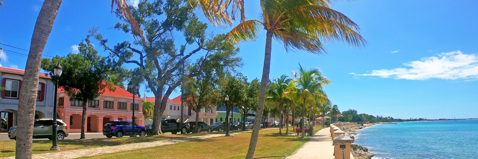 Promenade of Caribbean island along the coast with colorful buildings on a sunny day.