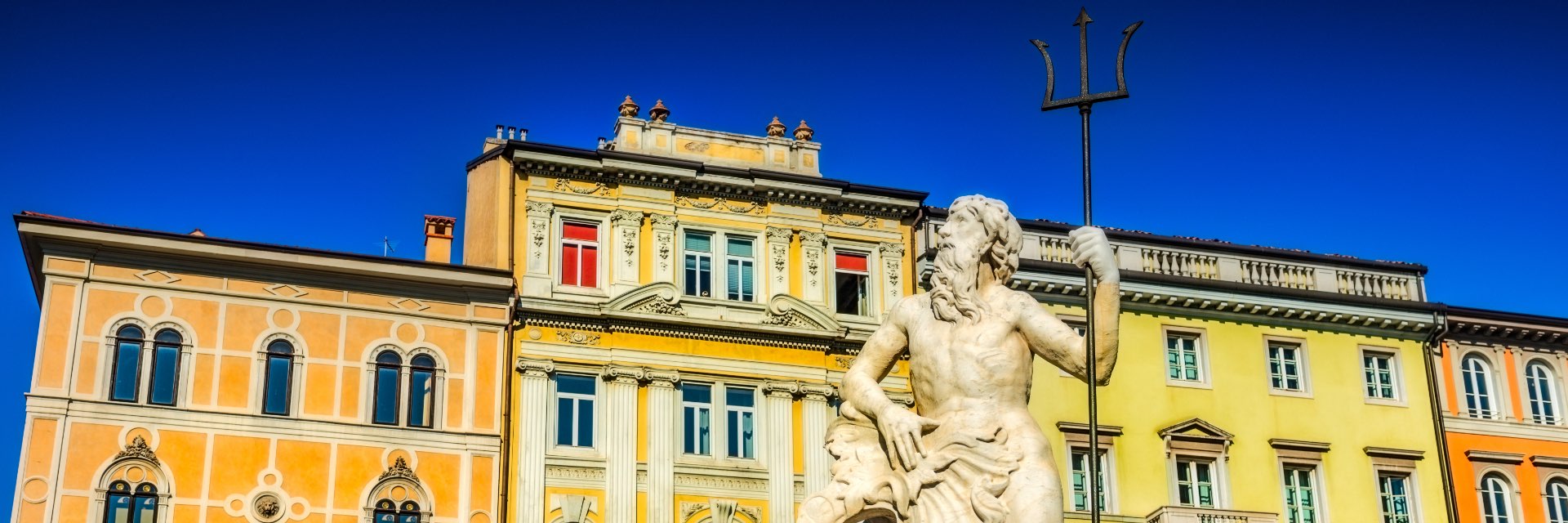 Houses in different shades of yellow sit behind a statue of a man.