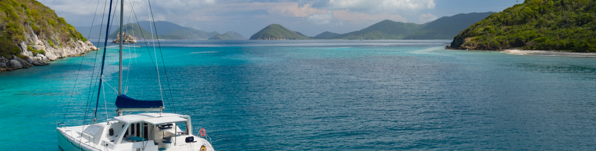 The landscape of a beach with crystal clear sea and a catamaran in the foreground.