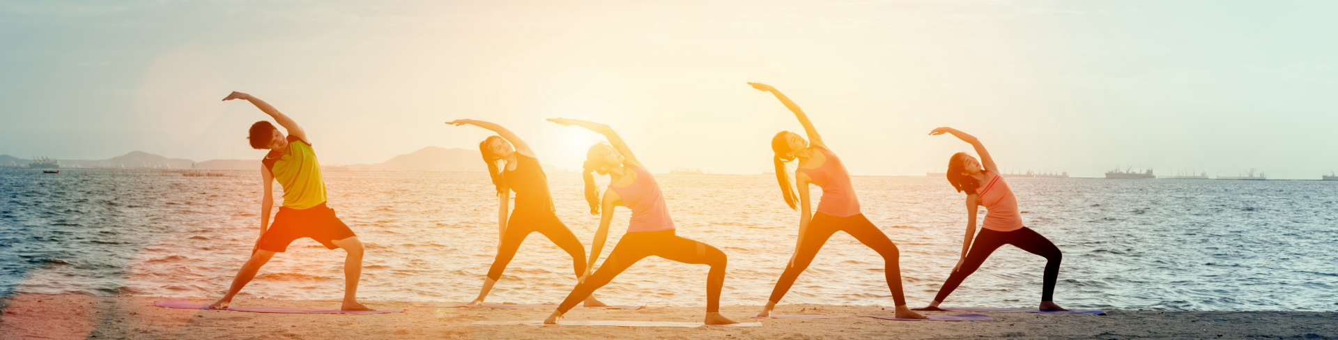 Five people doing yoga at dusk on the beach.