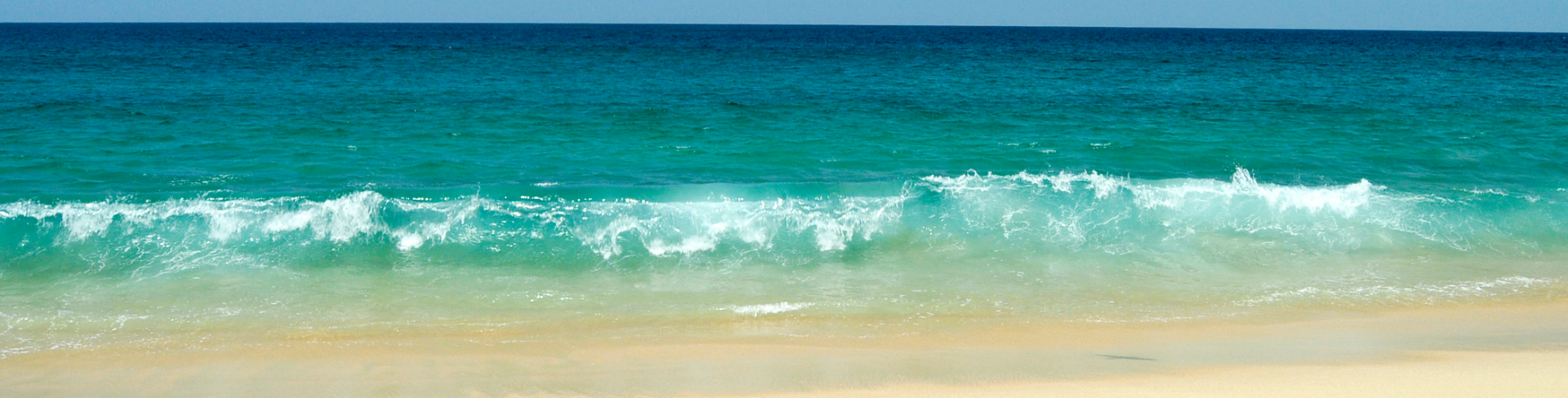 Blue waves of the ocean washing up on yellow sand beach.