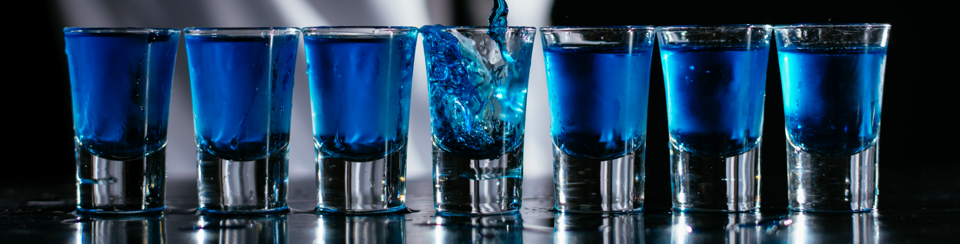 A series of shots that are filled by a bartender in a white shirt.