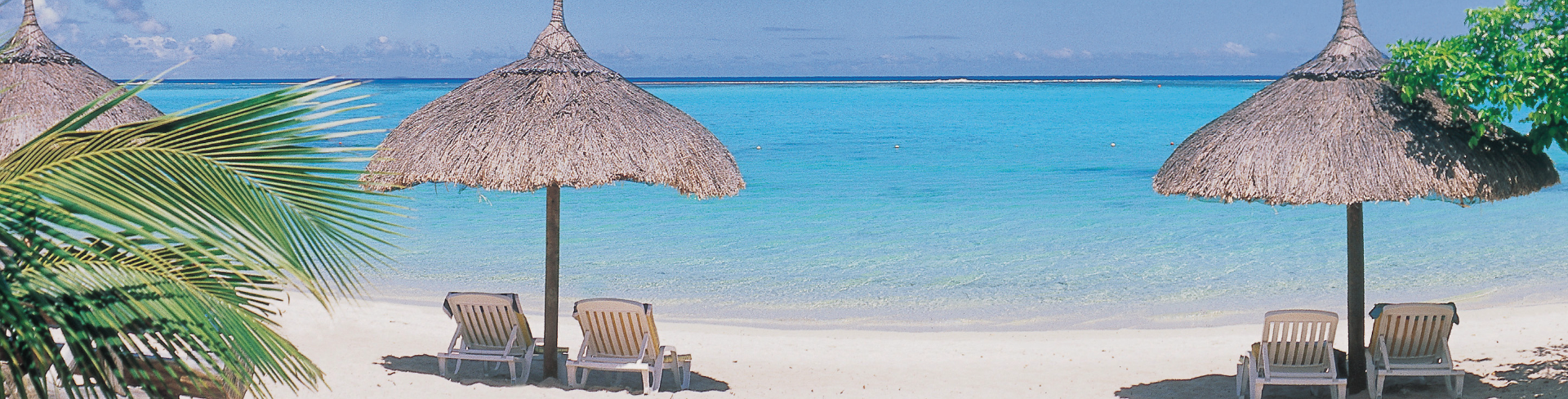 Two straw umbrellas with deckchairs in the middle of a beach with white sand and crystal clear sea.