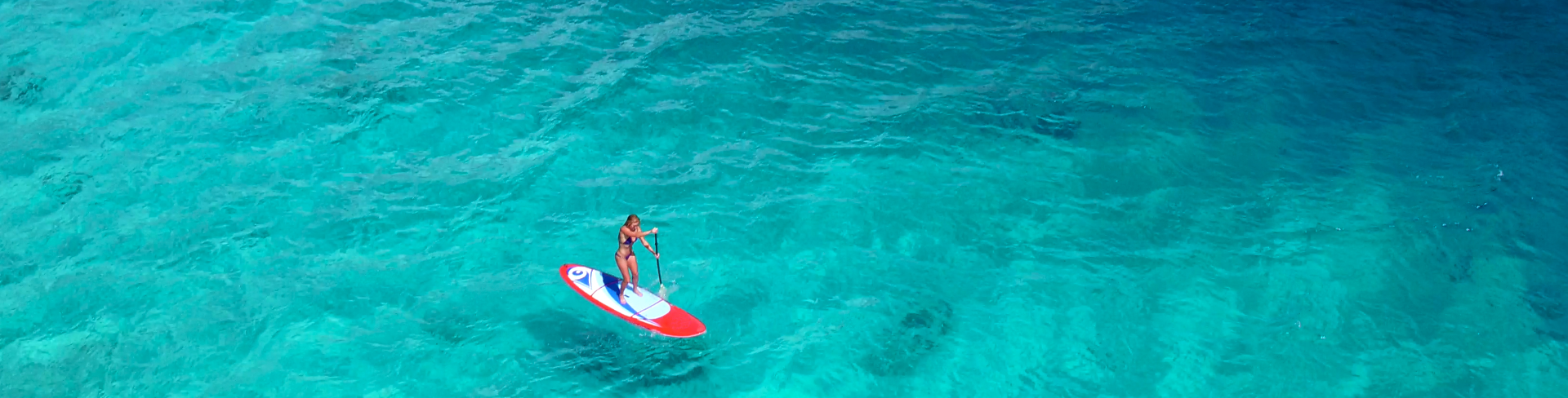 A woman doing sup only with an oar in a transparent sea.