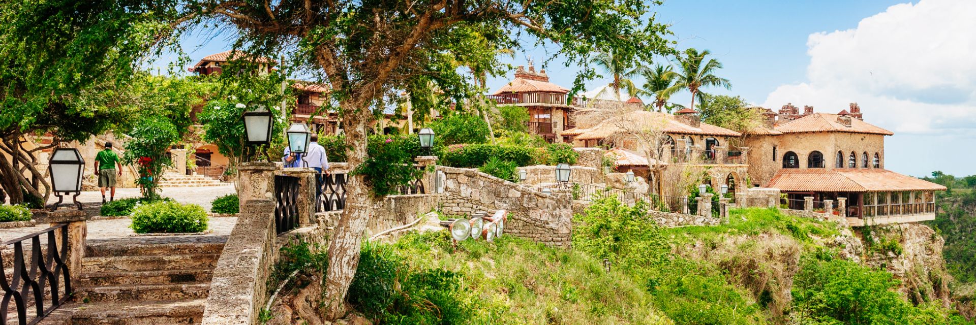 A stone path and wall lead to a stone building at the top of a high peak near La Romana