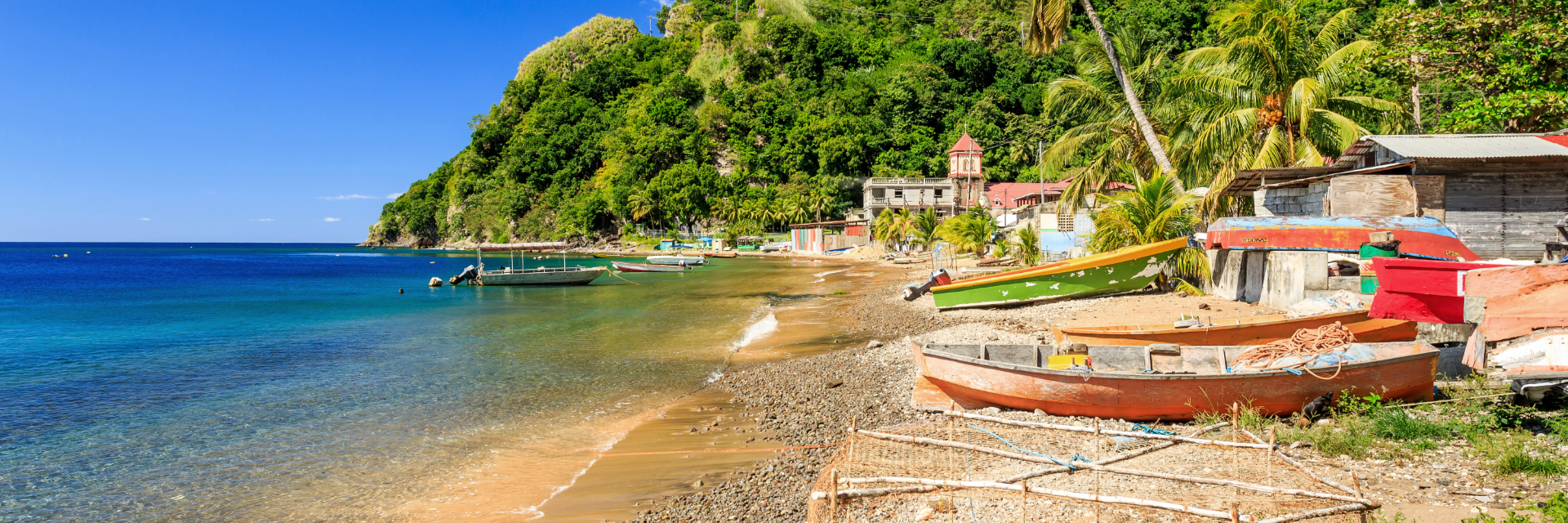 A red fishing boat sits ashore next to blue waters in front of a steep hill