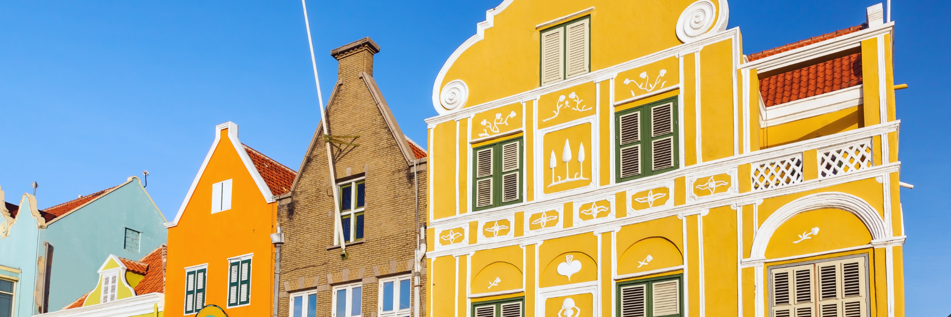 Orange stucco, tan brick, and bright yellow building facades with ornate white accent trim paint