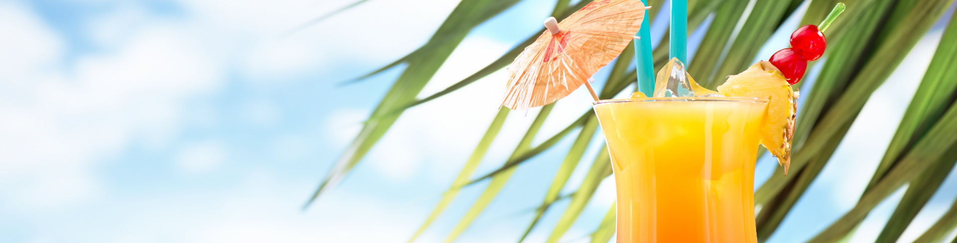 A tropical cocktail in a glass with a paper umbrella and cherries.