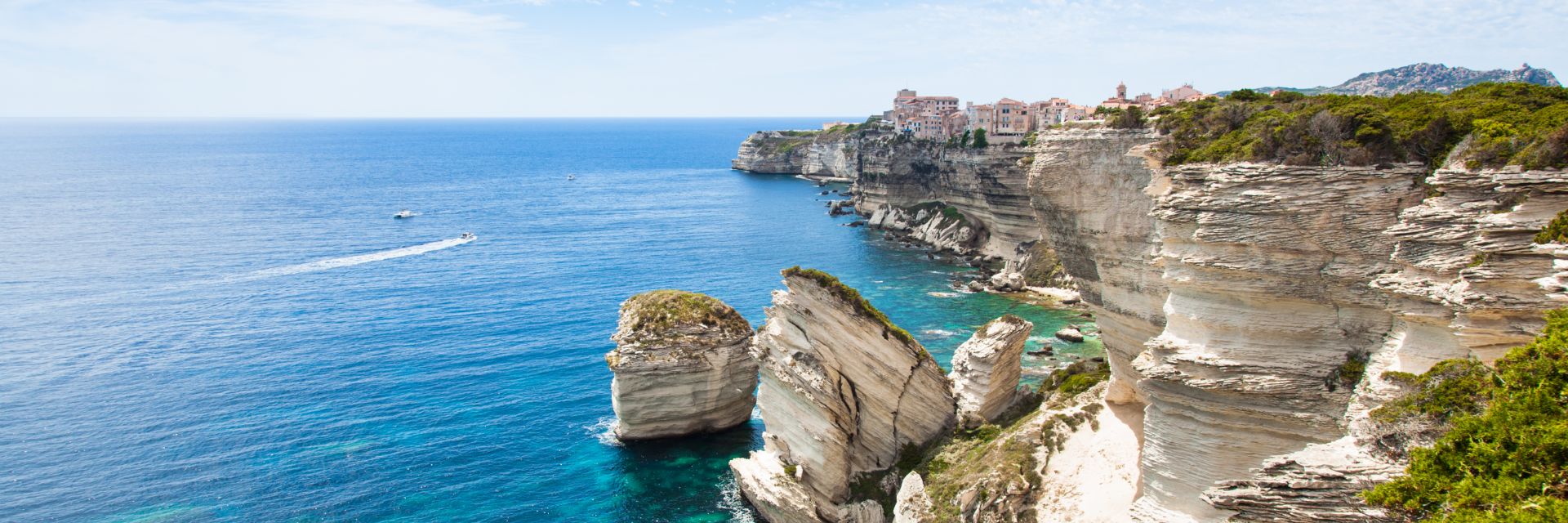 Tall white limestone cliffs rise above the sea, topped with the medieval town of Bonifacio.