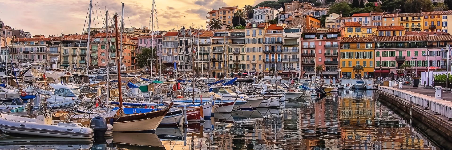 A harbor filled with sailboats at anchor with pastel houses in the background at dawn.
