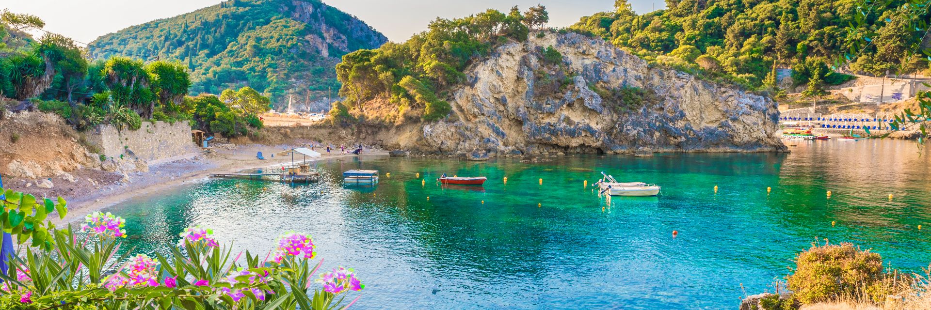 A secluded cove encircled by white limestone rocks covered in lush greenery and pink flowers.