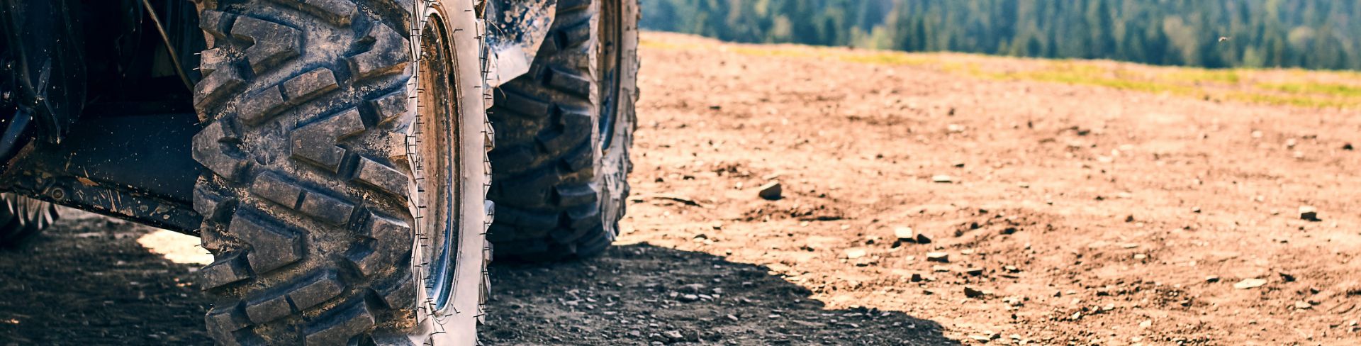 A close-up of the tires of a 4x4 on a dirt path with a forest in the background.