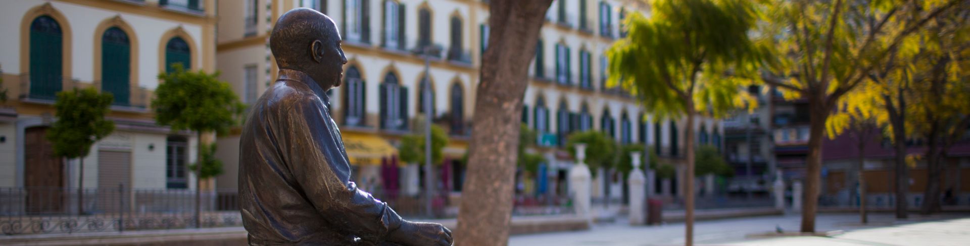 A bronze statue of Pablo Picasso sitting on a bench in a plaza.