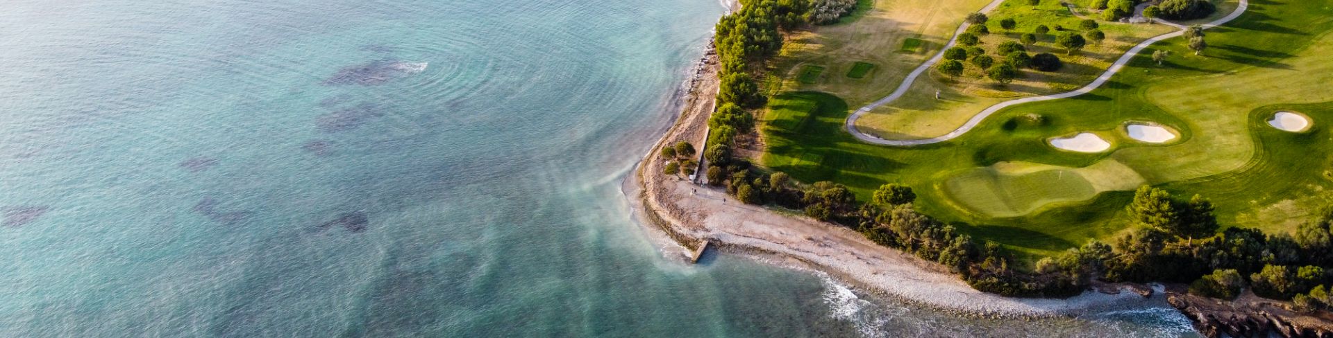 The aerial view of a groomed golf course on a beachy coastline.