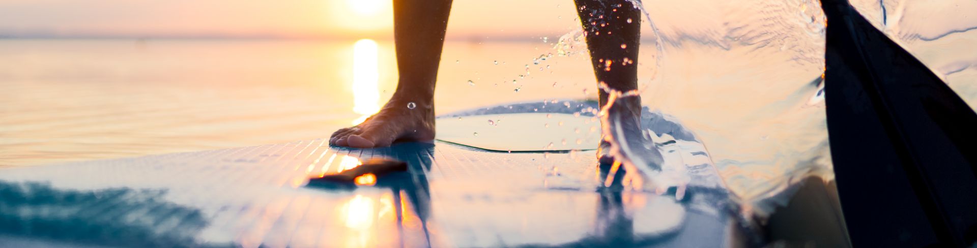 A person's legs standing on a paddle board with their oar splashing water to move forward.