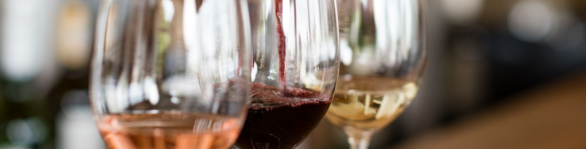A bottle of red wine being poured into a glass next to glasses of rosé and white wine.